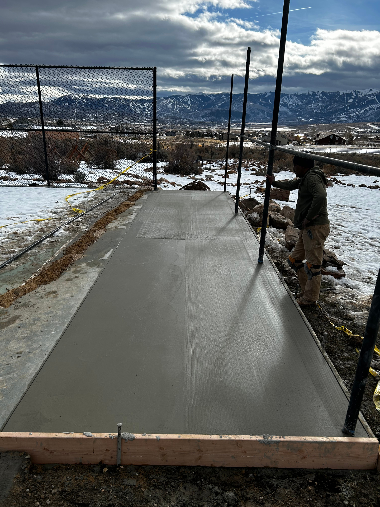 Concrete walkway beside batting cage with worker and Wasatch mountain backdrop